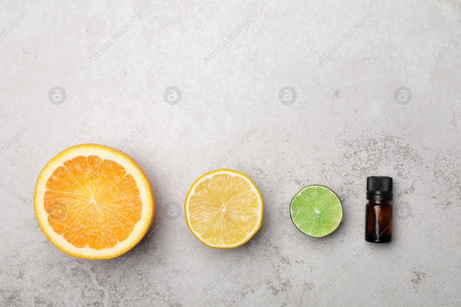 Photo of Bottle of citrus essential oil and fresh fruits on light table, flat lay. Space for text