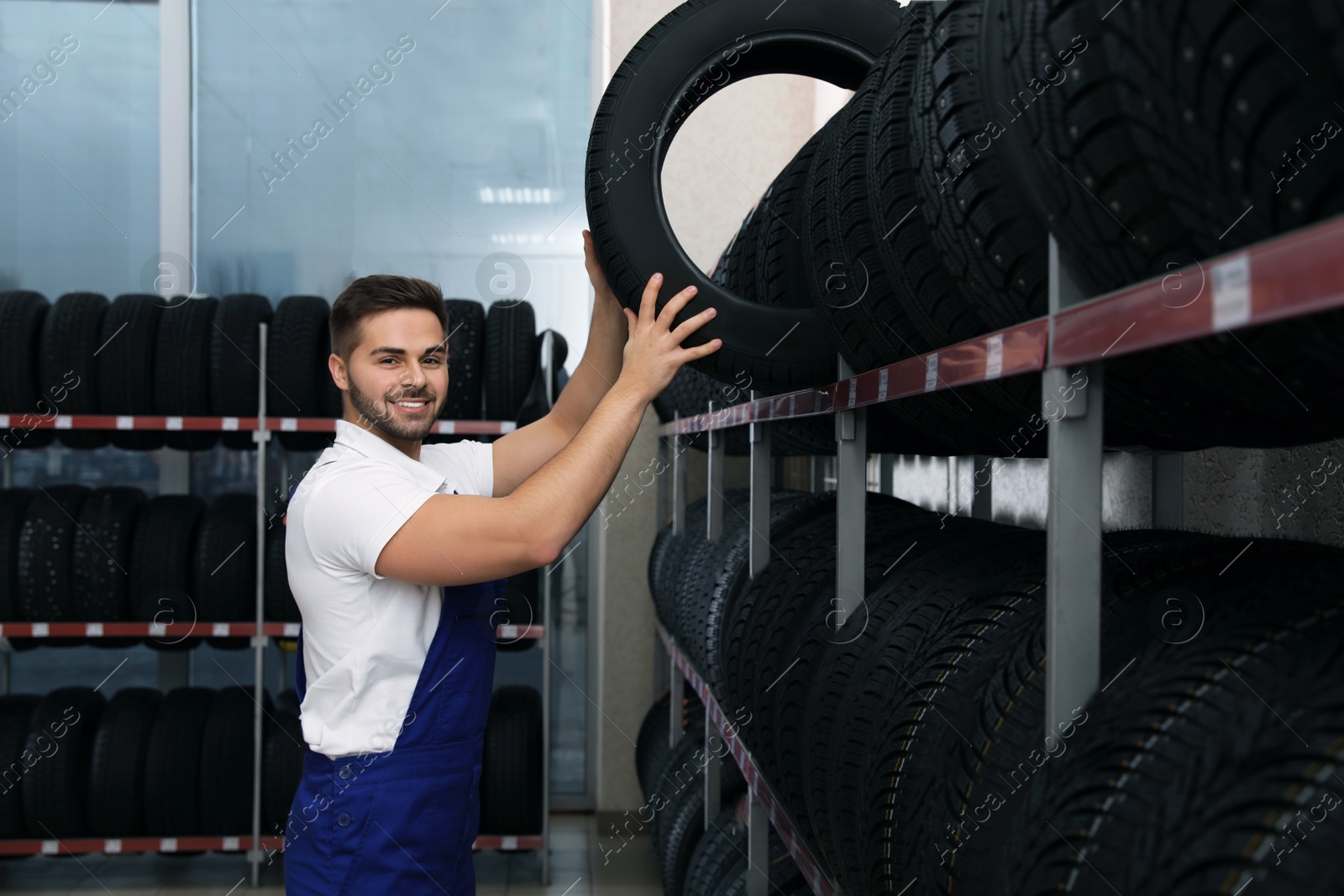 Photo of Male mechanic with car tire in auto store