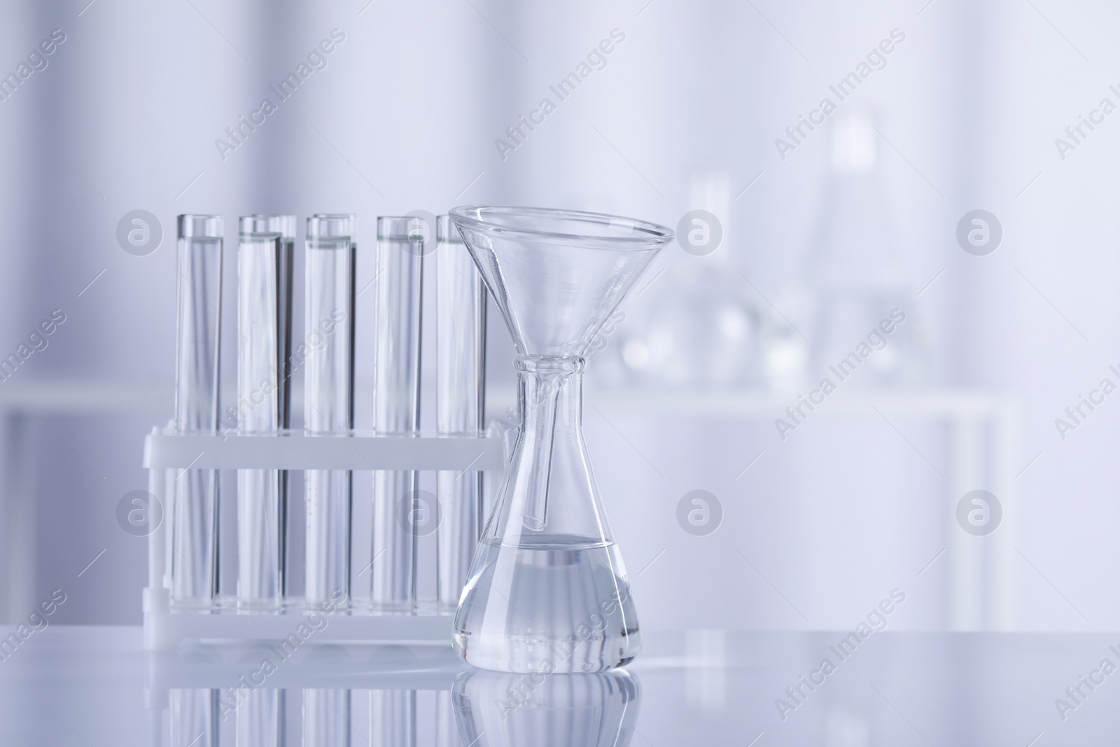 Photo of Different laboratory glassware with transparent liquid on table against blurred background. Space for text
