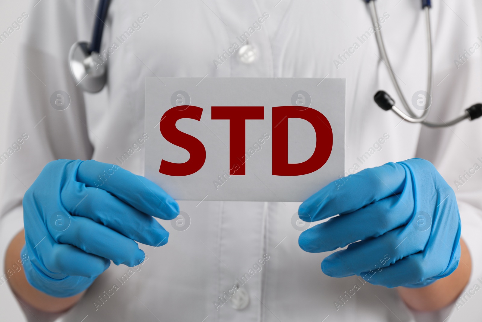 Photo of Doctor holding sheet of paper with abbreviation STD on white background, closeup