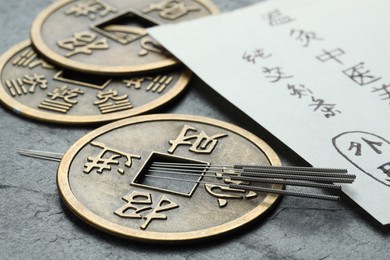 Photo of Acupuncture needles, Chinese coins and paper with characters on grey textured table, closeup