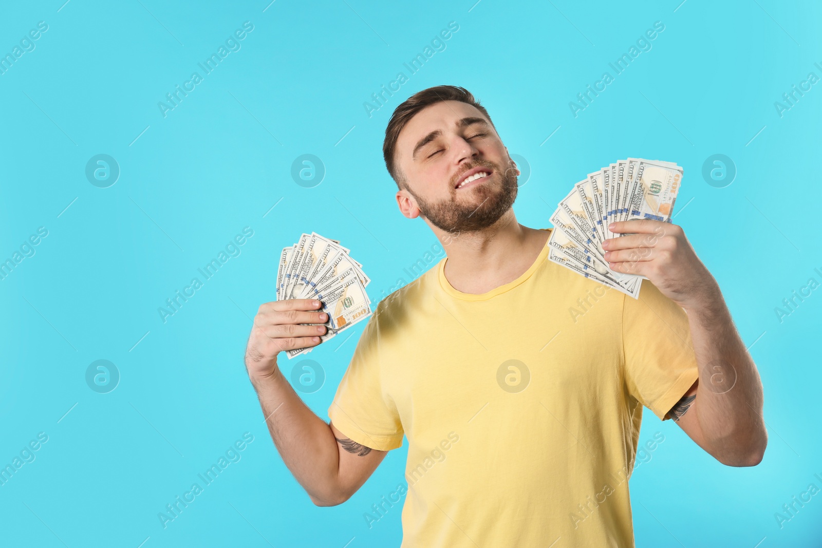 Photo of Happy young man fanning himself with money on color background. Space for text