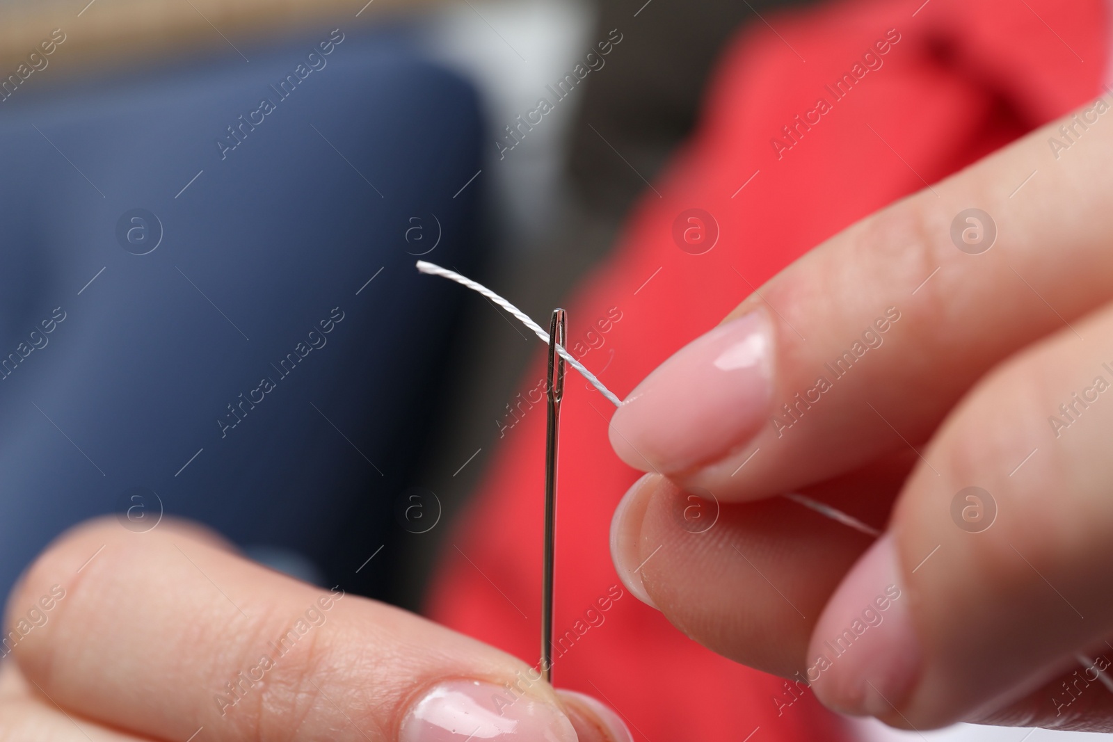 Photo of Woman inserting thread through eye of needle on blurred background, closeup