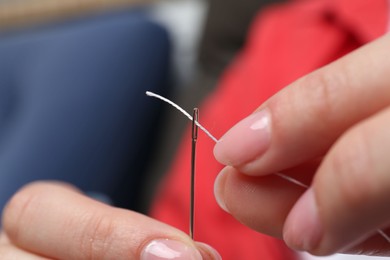 Photo of Woman inserting thread through eye of needle on blurred background, closeup