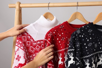 Photo of Woman choosing Christmas sweater from rack near light wall, closeup