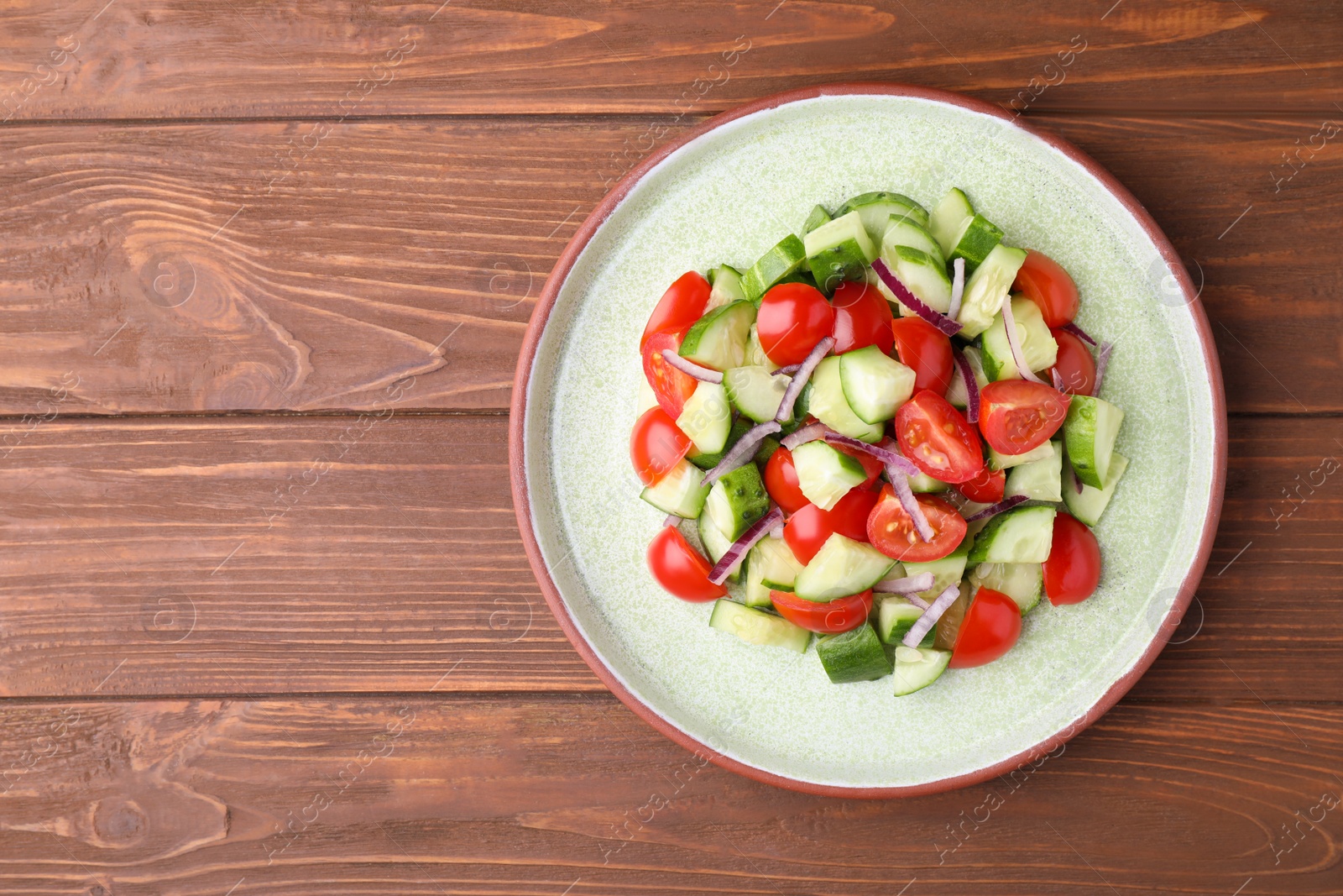 Photo of Plate with delicious fresh cucumber tomato salad on wooden table, top view. Space for text