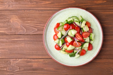 Photo of Plate with delicious fresh cucumber tomato salad on wooden table, top view. Space for text