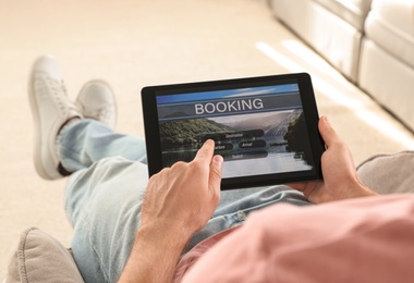 Man booking tickets online on sofa indoors, closeup. Travel agency concept