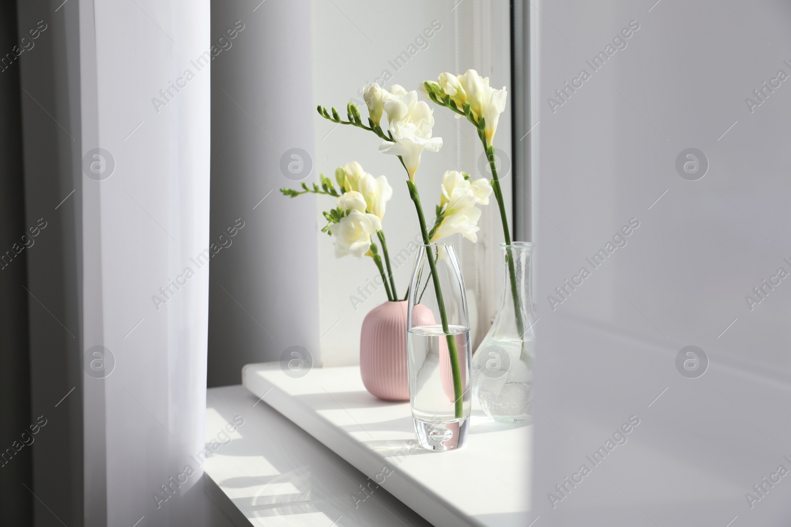 Photo of Beautiful white spring freesia flowers on window sill in room