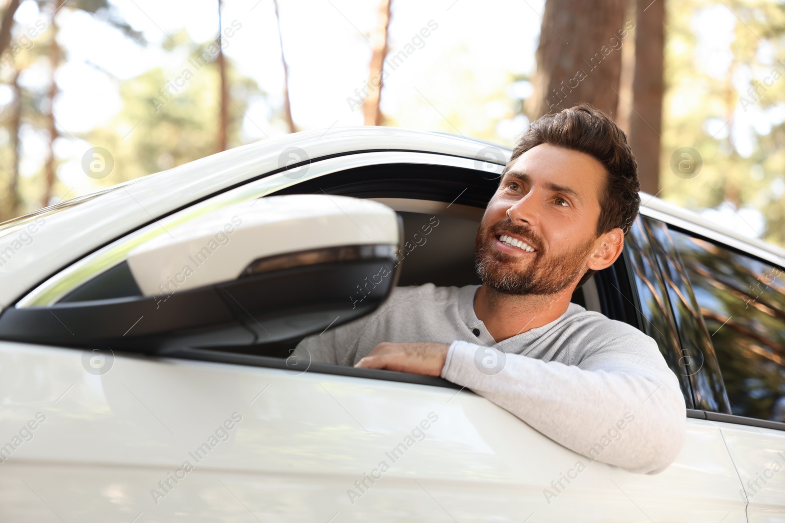 Photo of Happy bearded man looking out of car window, view from outside. Enjoying trip