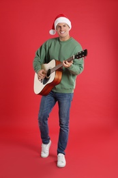 Photo of Man in Santa hat playing acoustic guitar on red background. Christmas music