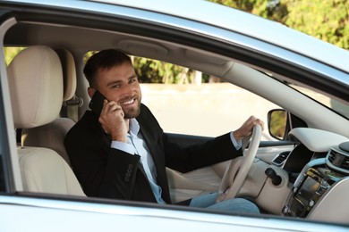 Photo of Handsome young driver talking on phone in modern car