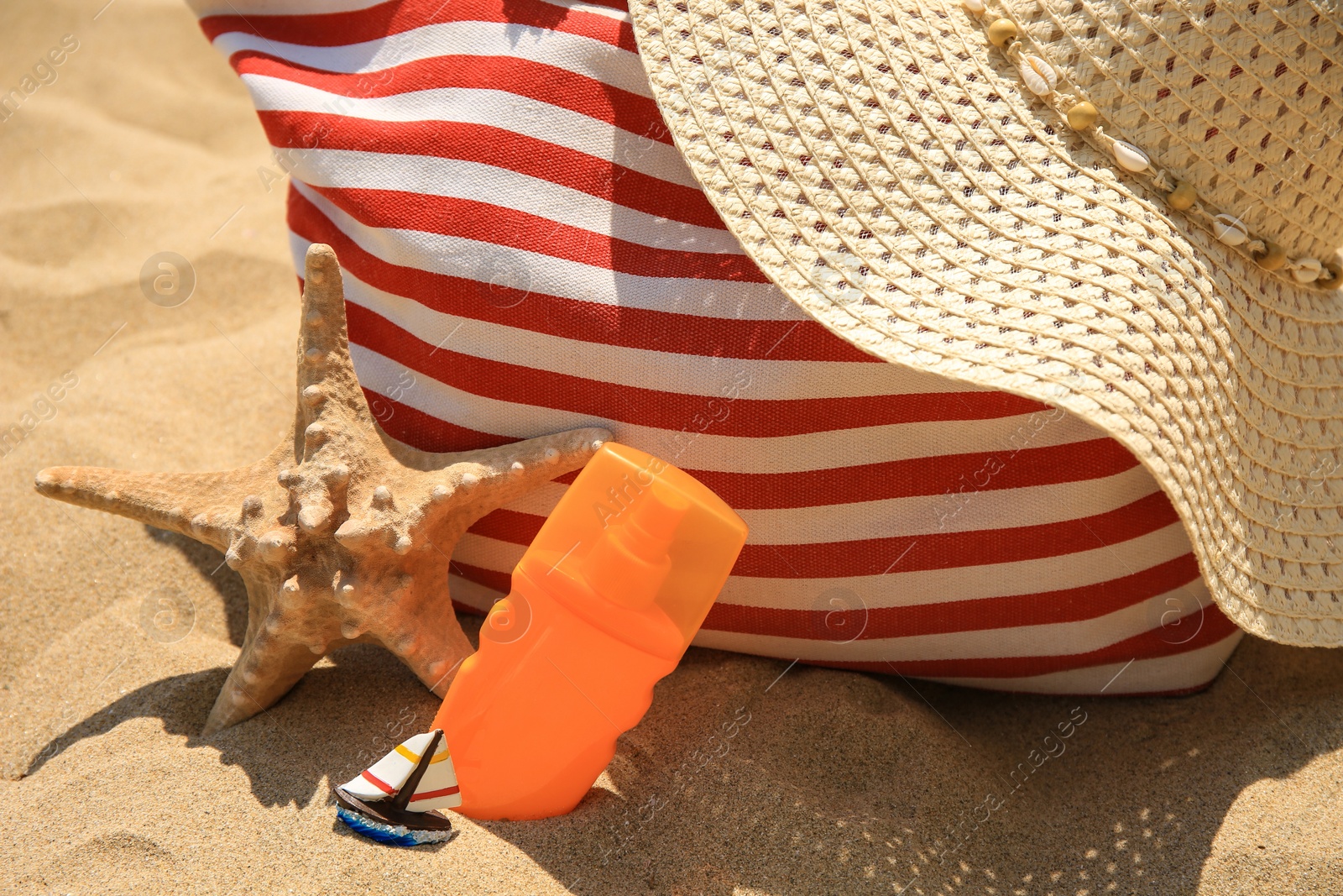 Photo of Bottle of sunscreen, starfish, bag and hat on sand, closeup. Sun protection care