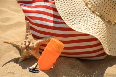 Photo of Bottle of sunscreen, starfish, bag and hat on sand, closeup. Sun protection care