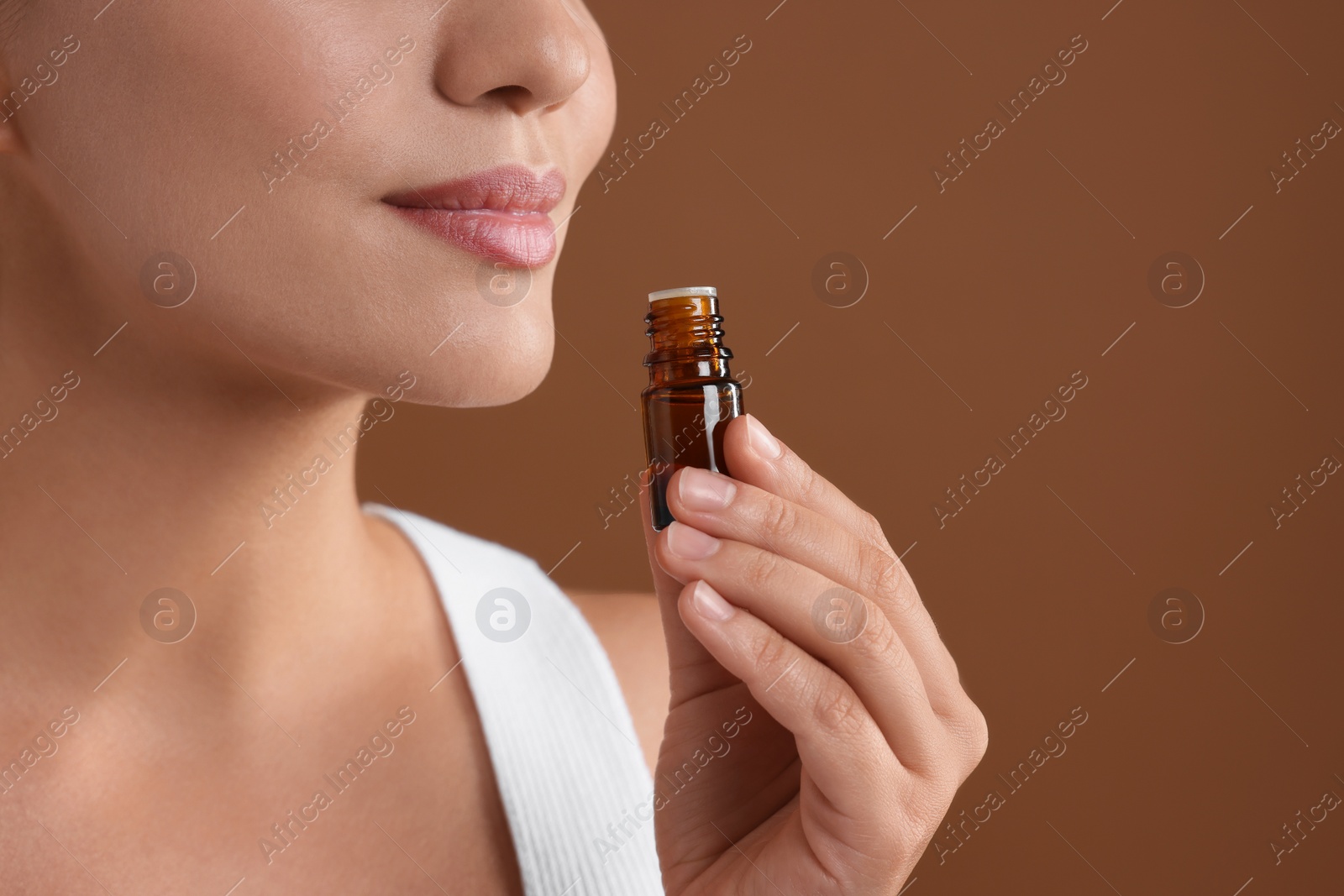 Photo of Woman with bottle of essential oil on brown background, closeup. Space for text