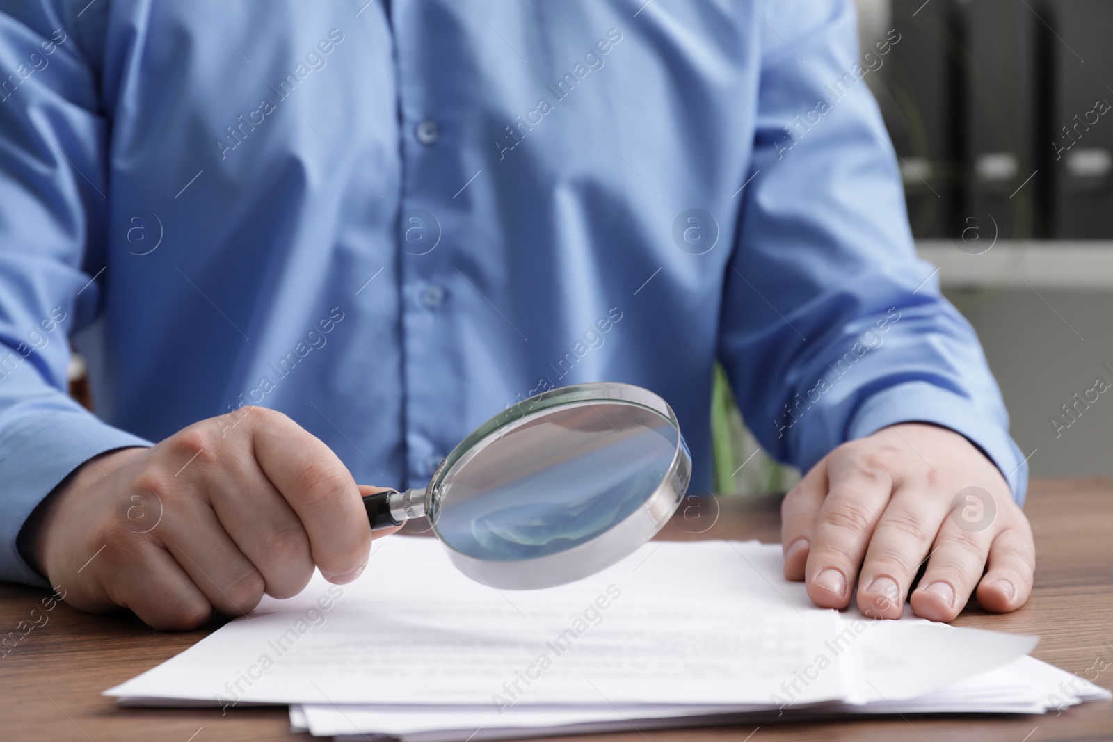 Photo of Man looking at document through magnifier at wooden table, closeup. Searching concept