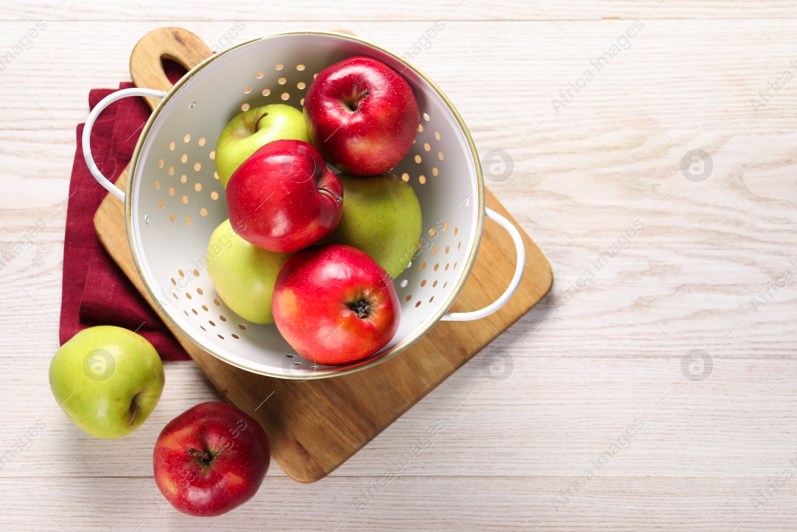 Photo of Fresh apples in colander on white wooden table, flat lay. Space for text