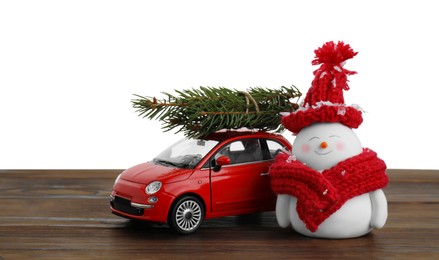 Photo of Cute decorative snowman, toy car and fir tree branches on wooden table against white background