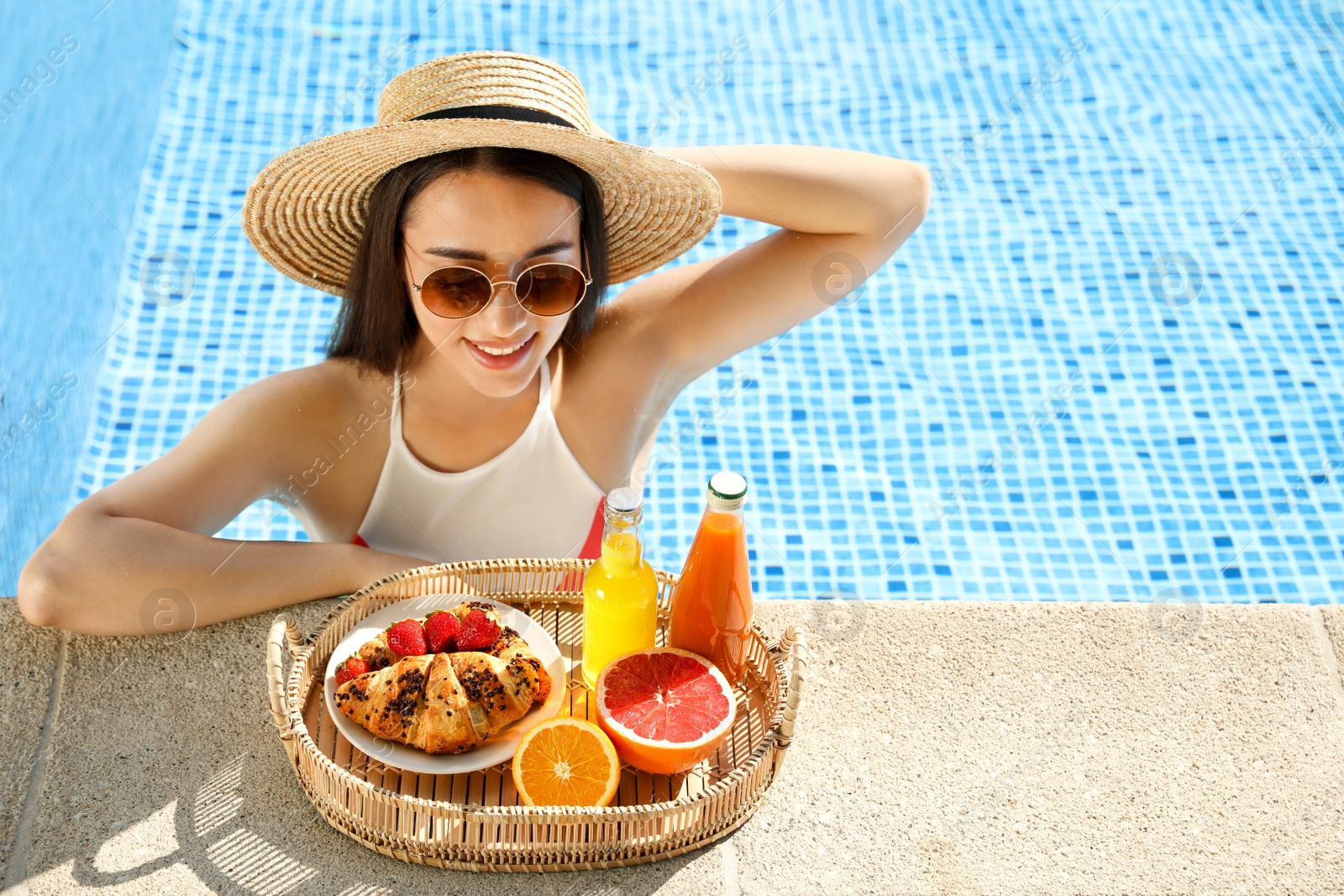 Photo of Young woman with delicious breakfast on tray in swimming pool. Space for text