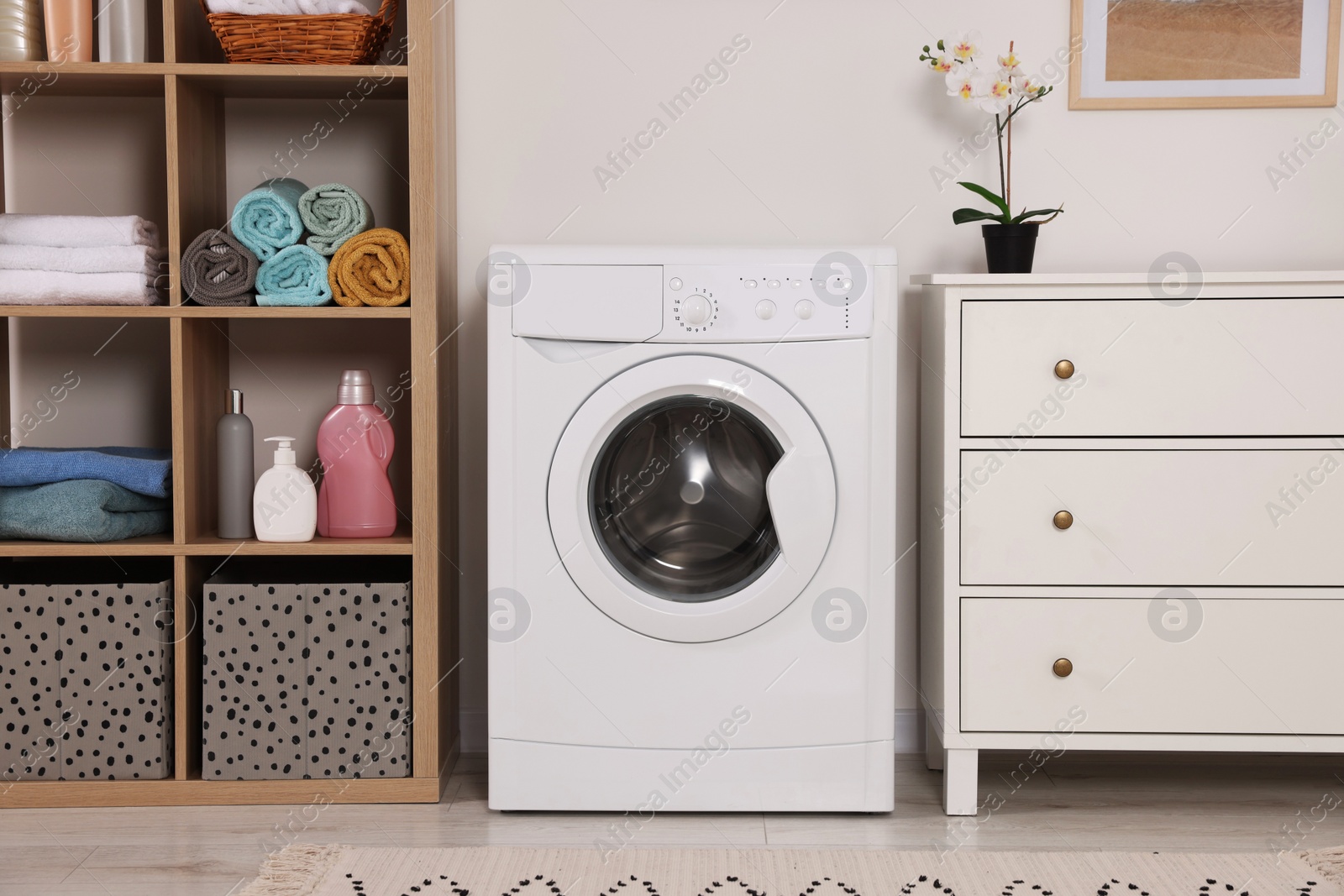 Photo of Stylish laundry room with washing machine and chest of drawers. Interior design