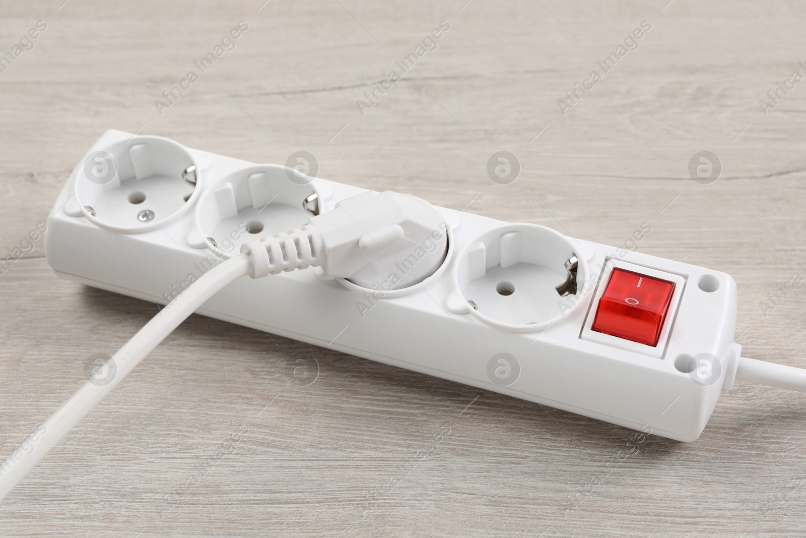 Photo of Power strip with extension cord on white wooden floor, closeup. Electrician's equipment