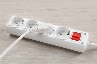 Power strip with extension cord on white wooden floor, closeup. Electrician's equipment