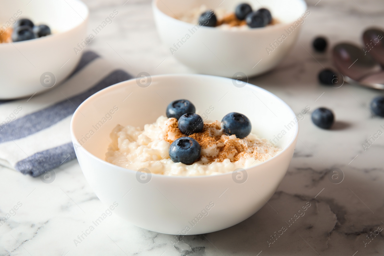 Photo of Creamy rice pudding with cinnamon and blueberries in bowl on marble table