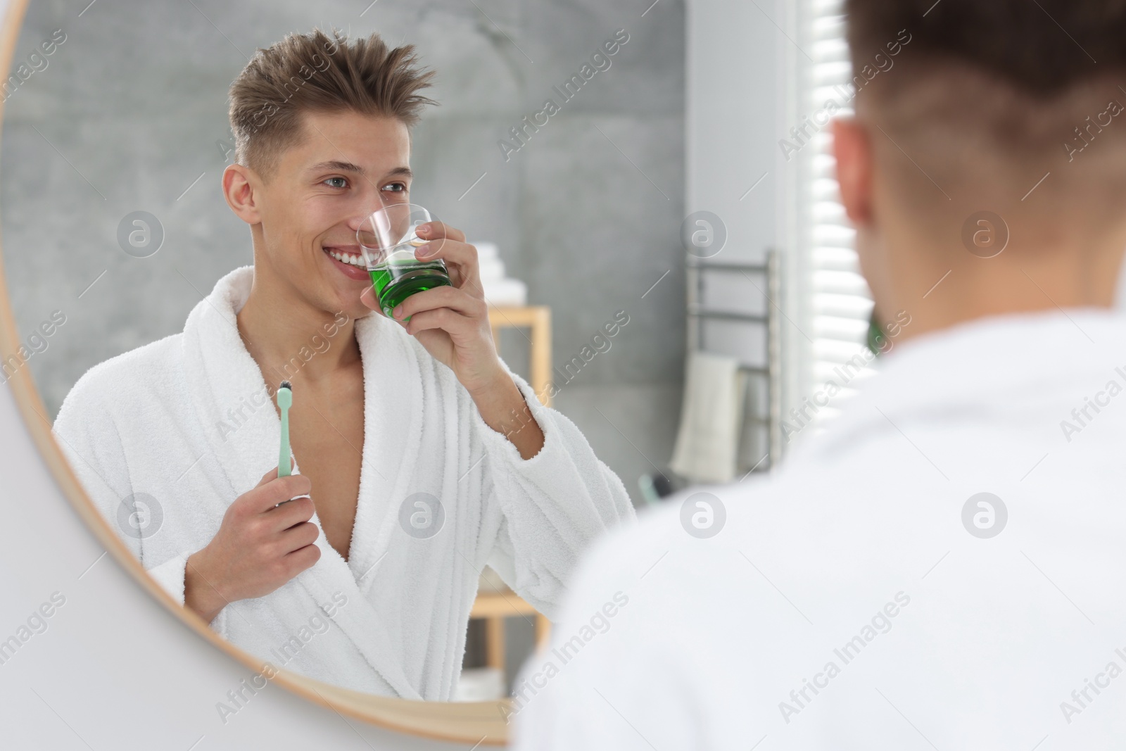 Photo of Young man using mouthwash near mirror in bathroom