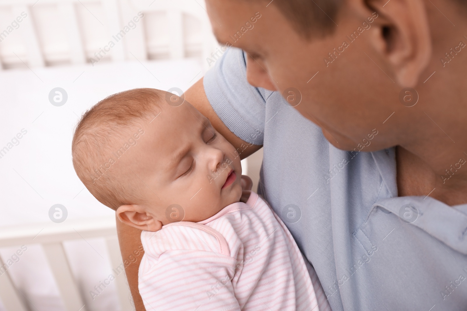 Photo of Happy father with his cute sleeping baby near crib indoors, closeup