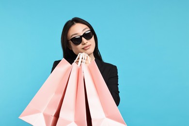 Beautiful woman with shopping bags on light blue background. Space for text