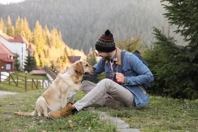 Photo of Happy man and adorable dog sitting on green grass in mountains. Traveling with pet