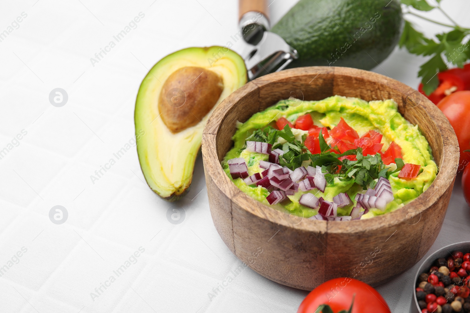 Photo of Bowl of delicious guacamole with onion, tomatoes and ingredients on white tiled table. Space for text