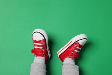 Little child in stylish red gumshoes on green background, top view