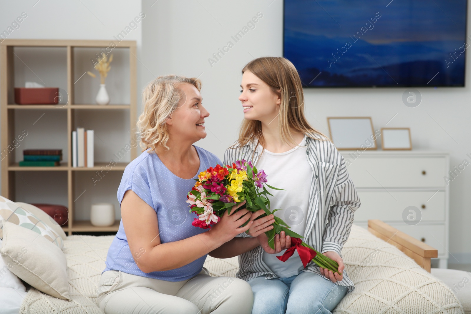 Photo of Young daughter congratulating her mom with flowers at home. Happy Mother's Day