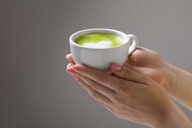 Woman with cup of delicious matcha latte on light grey background, closeup