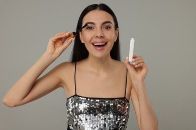 Photo of Beautiful young woman applying mascara on grey background