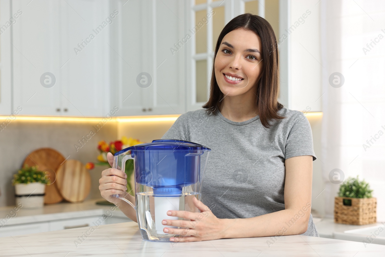 Photo of Woman with filter jug of water in kitchen