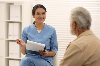 Photo of Smiling nurse with clipboard consulting elderly patient in hospital
