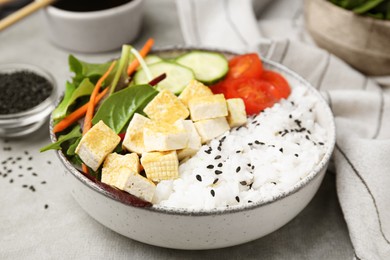 Delicious poke bowl with vegetables, tofu and mesclun on light grey table, closeup