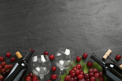 Bottles of red wine, glasses and grapes on black table, flat lay. Space for text