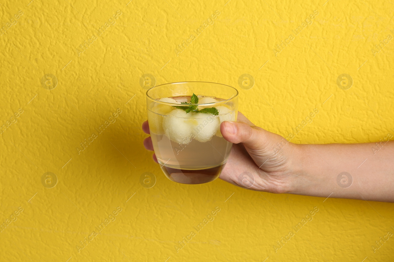 Photo of Woman holding glass of melon ball cocktail with mint against yellow background