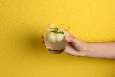 Woman holding glass of melon ball cocktail with mint against yellow background