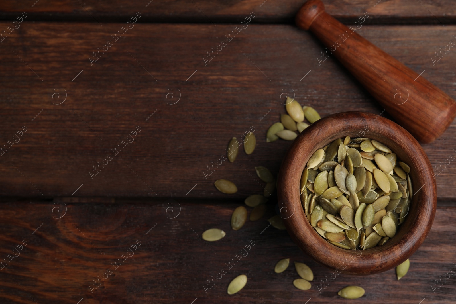 Photo of Mortar with pumpkin seeds and pestle on wooden table, flat lay. Space for text