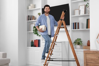 Photo of Happy man with books on wooden folding ladder at home