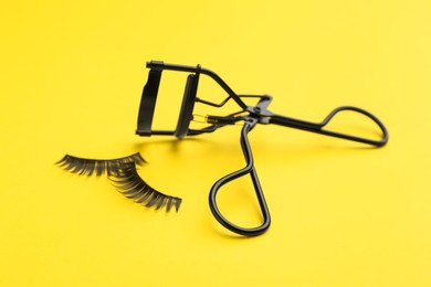 Photo of False eyelashes and curler on yellow background