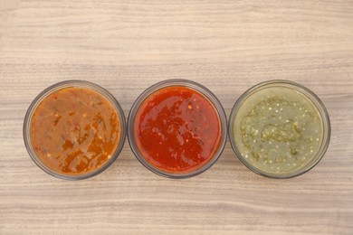 Photo of Different tasty salsa sauces on wooden table, flat lay
