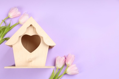 Beautiful bird house and pink tulips on violet background, flat lay. Space for text