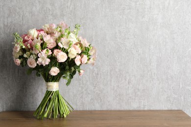 Beautiful bouquet of fresh flowers on wooden table near grey wall, space for text