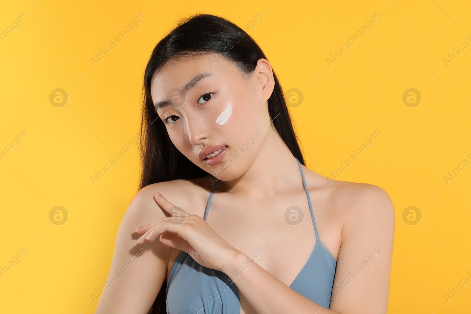 Photo of Beautiful young woman with sun protection cream on her face against orange background