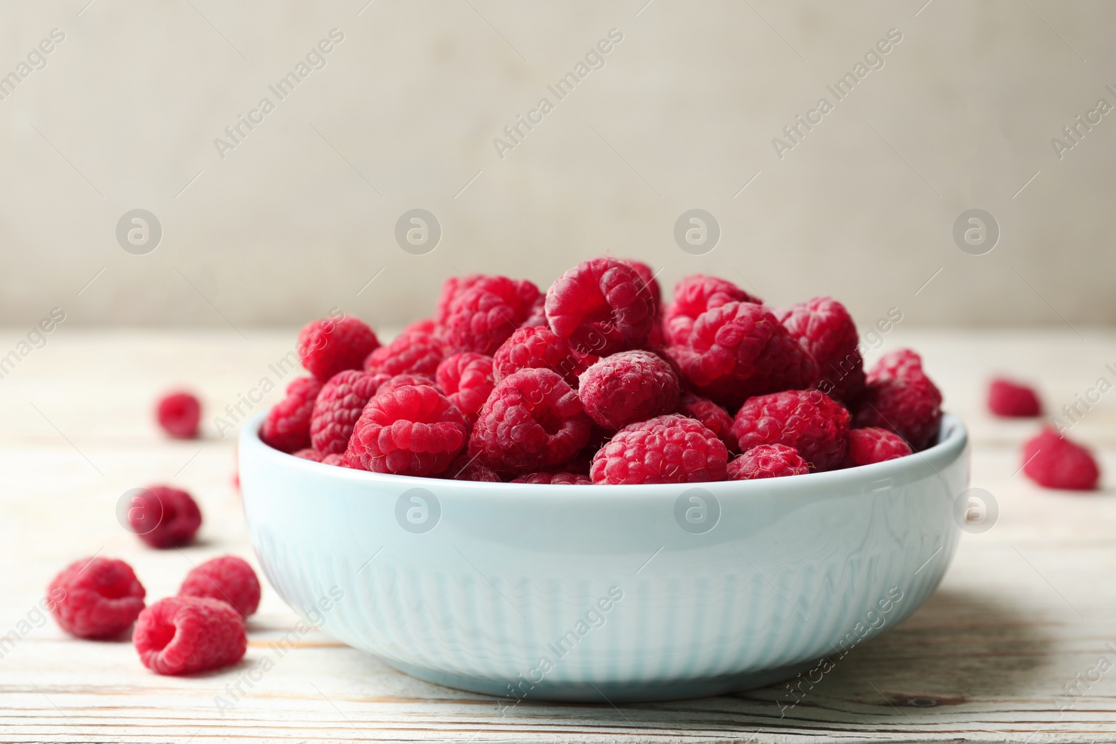 Photo of Bowl of delicious fresh ripe raspberries on white wooden table, space for text